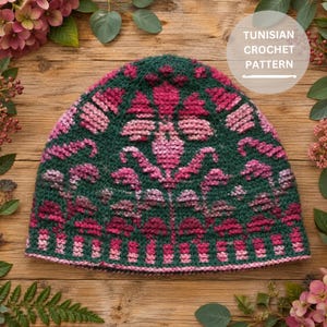 May include: A beanie featuring a Tunisian crochet pattern with a dark green background and a symmetrical floral design in shades of pink and magenta. The text TUNISIAN CROCHET PATTERN is visible in a white circular overlay on the upper right side.