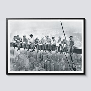 Pode incluir: Uma fotografia a preto e branco de um grupo de trabalhadores da construção civil sentados numa viga de aço muito acima da cidade. Os trabalhadores estão a almoçar e a olhar para a vista. O horizonte da cidade é visível no fundo.