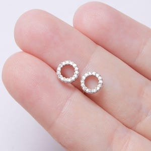 May include: A pair of silver stud earrings with a circle design. The circle is outlined with small, clear cubic zirconia stones.
