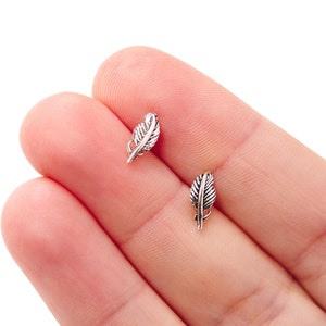 May include: A pair of silver feather earrings. The earrings are small and delicate, and they have a simple, elegant design.