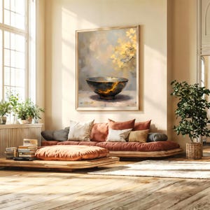 Puede incluir: Un salón con un cuadro enmarcado de un cuenco negro con detalles dorados. La habitación incluye un sofá bajo con cojines, suelo de madera y una planta en maceta. La paleta de colores es neutra con tonos cálidos.