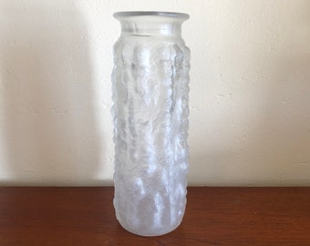 May include: A clear glass vase with a textured surface. The vase is cylindrical and has a rounded top.