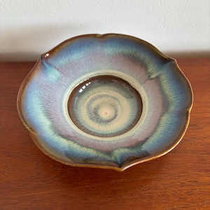 May include: A small, scalloped ceramic bowl with a blue, green, and brown glaze. The bowl has a swirling pattern in the centre.