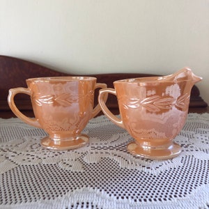 May include: A set of two vintage milk glass creamer and sugar bowl in a peach colour with a leaf design.
