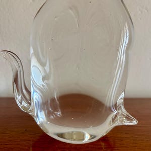 May include: A clear glass pitcher with a curved spout and a rounded body. The pitcher is made of transparent glass, allowing light to pass through. The design is simple and elegant, suitable for serving beverages.