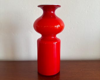 Op de afbeelding: Een rode glazen vaas met een bolvormig middengedeelte en een cilindrische basis.