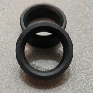 May include: Two black rubber rings, one slightly overlapping the other. The rings have a circular shape with a hollow center. The image is taken from a slightly elevated angle, showing the top of the rings.