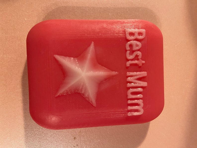 May include: A pink square-shaped soap with a white star and the text "Best Mum" embossed on the front.