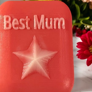May include: A red square-shaped gift with the words "Best Mum" embossed in white lettering and a white star in the centre.