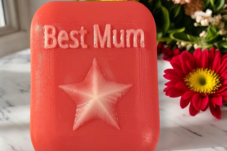May include: A red square-shaped gift with the words "Best Mum" embossed in white lettering and a white star in the centre.