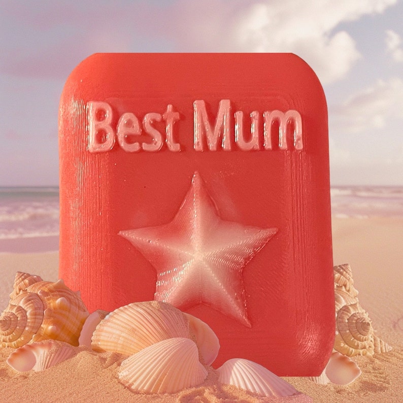 May include: A red square with the words "Best Mum" in white lettering and a white star in the centre. The square is sitting on a beach with seashells.