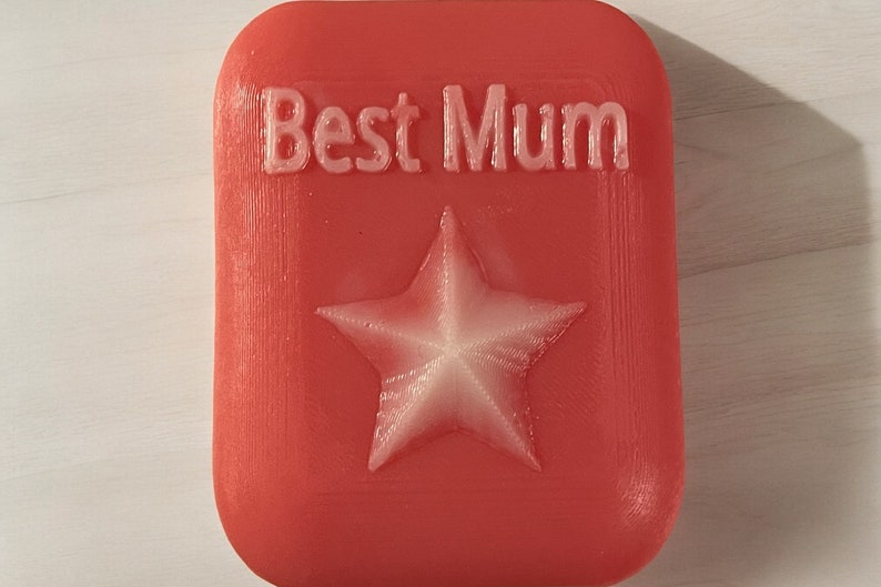 May include: A red rectangular soap with the words "Best Mum" embossed in white and a white five-pointed star in the centre.