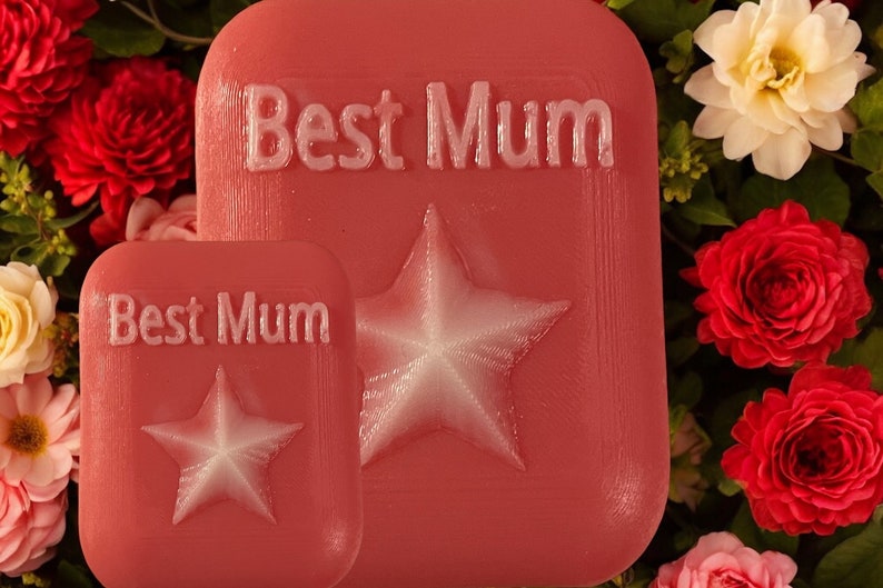 May include: Two pink rectangular plaques with the text "Best Mum" and a white star embossed on each. The plaques are surrounded by red and white flowers.