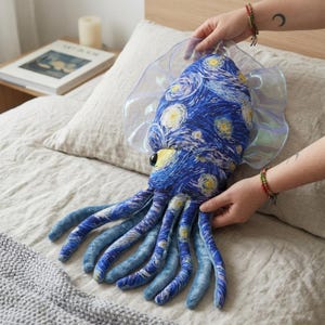 Könnte beinhalten: Ein Plüsch-Tintenfisch-Spielzeug mit einem blau-gelben Sternennacht-Design. Das Spielzeug hat große Augen und durchscheinende, irisierende Flossen. Die Tentakel haben einen Farbverlauf in Blautönen. Das Spielzeug ist etwa 46 cm lang.