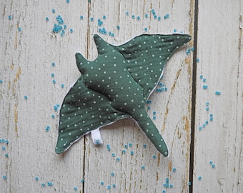 May include: A green and white polka dot fabric stingray stuffed animal with white trim. The stingray is lying on a white wooden surface.
