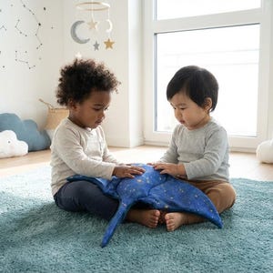 K&ouml;nnte beinhalten: Zwei kleine Kinder sitzen auf einem blauen Teppich und interagieren mit einem blauen Pl&uuml;schtier mit Sternenmuster. Der Raum hat ein himmlisches Thema mit wolkenf&ouml;rmigen Kissen und Sternaufklebern an der Wand. Ein Fenster sorgt f&uuml;r nat&uuml;rliches Licht.