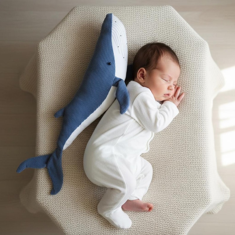 Peut inclure: Un nourrisson endormi en barboteuse blanche repose &agrave; c&ocirc;t&eacute; d'une peluche en forme de baleine bleue et blanche. La peluche est faite d'un tissu textur&eacute;, semblable &agrave; du velours c&ocirc;tel&eacute;. Le b&eacute;b&eacute; est sur une couverture cr&egrave;me textur&eacute;e.