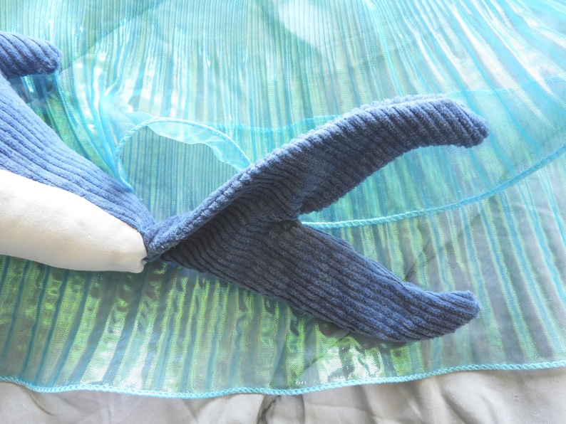 Peut inclure: Un jouet en forme de baleine bleue en peluche avec un ventre blanc et une texture en velours c&ocirc;tel&eacute;. La queue de la baleine est incurv&eacute;e et pos&eacute;e sur un tissu bleu iris&eacute; et chatoyant. Le jouet est con&ccedil;u pour ressembler &agrave; une baleine.