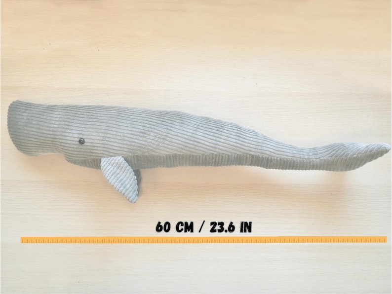 K&ouml;nnte beinhalten: Ein graues Cord-Wal-Pl&uuml;schtier, ca. 60 cm lang, mit kleiner Flosse und Knopfauge. Das Spielzeug liegt auf einer hellen Holzoberfl&auml;che. Der K&ouml;rper des Wals hat eine gerippte Textur.
