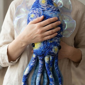 Puede incluir: Un peluche de pulpo con el cuadro "La noche estrellada" de Van Gogh. El dise&ntilde;o azul y amarillo cubre el cuerpo y los tent&aacute;culos. El juguete tiene un cuello con volantes e iridiscente.