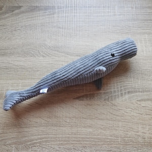 K&ouml;nnte beinhalten: Ein graues Cordwal-Pl&uuml;schtier mit kleiner Flosse und Schwanz. Der Wal hat ein kleines schwarzes Auge und ein kleines Etikett an der Seite. Das Spielzeug ist etwa 46 cm lang.