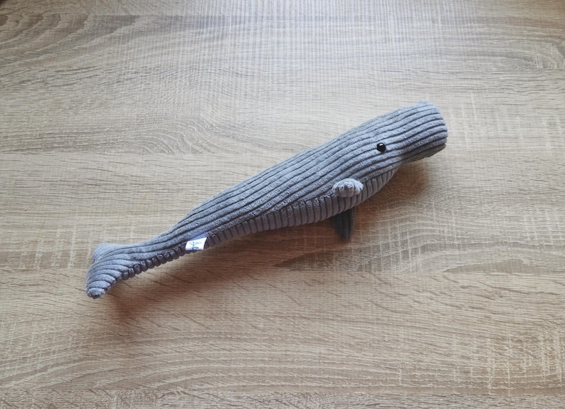 K&ouml;nnte beinhalten: Ein graues Cordwal-Pl&uuml;schtier mit kleiner Flosse und Schwanz. Der Wal hat ein kleines schwarzes Auge und ein kleines Etikett an der Seite. Das Spielzeug ist etwa 46 cm lang.
