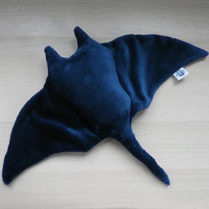 K&ouml;nnte beinhalten: Ein dunkelblaues Pl&uuml;sch-Manta-Rochen-Spielzeug mit weicher, samtiger Textur. Das Spielzeug hat fl&uuml;gelartige Flossen und einen langen Schwanz. Ein kleines wei&szlig;es Etikett ist an einer der Flossen befestigt.