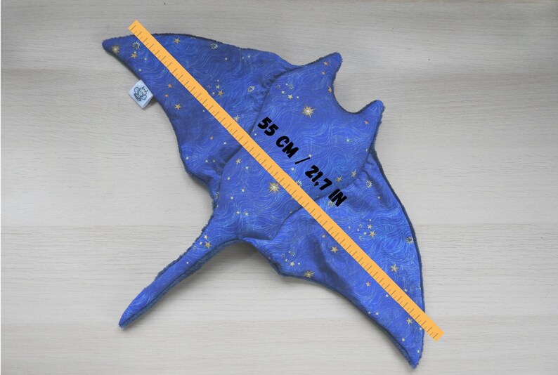 K&ouml;nnte beinhalten: Ein blaues Pl&uuml;schtier in Form eines Mantarochens mit Sternenmuster und einer Gr&ouml;&szlig;e von 55 cm. Das Spielzeug besteht aus weichem Stoff und hat ein detailliertes Design, einschlie&szlig;lich Flossen und Schwanz. Das Spielzeug ist 55 cm lang.