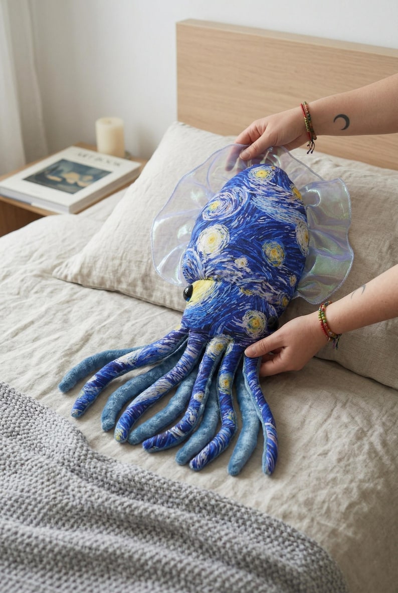 Puede incluir: Un peluche de calamar con un dise&ntilde;o de noche estrellada azul y amarillo. El juguete tiene ojos grandes y aletas transl&uacute;cidas e iridiscentes. Los tent&aacute;culos son un degradado de tonos azules. El juguete mide unos 46 cm de largo.