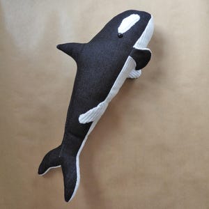 Könnte beinhalten: Ein handgefertigter Plüschwal in Schwarz und Weiß. Das Spielzeug hat einen dunklen, jeansartigen Stoff für den Körper und weißen Cord für den Bauch und die Akzente. Der Orca hat ein kleines schwarzes Auge und eine Flosse.