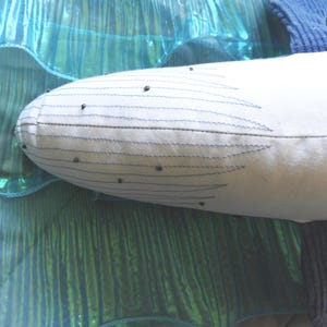 Peut inclure: Un jouet en peluche en forme de baleine blanche avec des d&eacute;tails cousus en bleu et de petits accents noirs. La baleine est plac&eacute;e sur un fond de tissu turquoise chatoyant, cr&eacute;ant un th&egrave;me aquatique et fantaisiste.