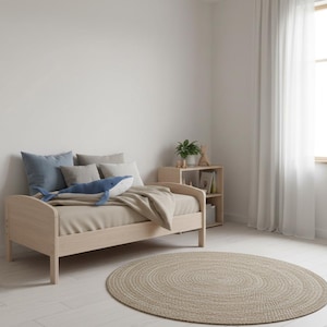 Peut inclure: Un lit en bois clair avec un matelas beige, des oreillers et une couverture. Un jouet en peluche baleine bleue repose sur le lit. Un tapis rond beige tress&eacute; est pos&eacute; sur le sol. Une petite table de chevet en bois avec une plante et des livres est visible.