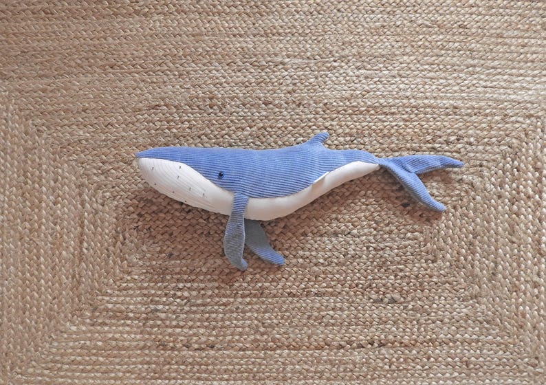 Peut inclure: Une peluche baleine bleue et blanche avec un corps textur&eacute; en forme de velours c&ocirc;tel&eacute;. Le jouet a un ventre blanc et un petit &oelig;il bleu fonc&eacute;. Il est pos&eacute; sur un tapis beige tiss&eacute;.