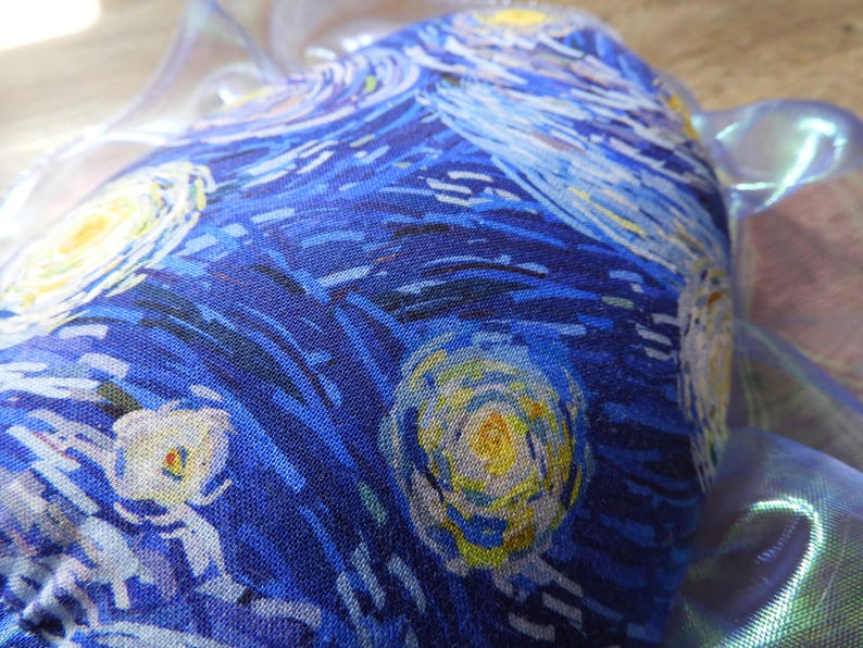 Puede incluir: Primer plano de un art&iacute;culo de tela con un estampado de "La noche estrellada" de Van Gogh. El dise&ntilde;o incluye pinceladas azules, amarillas y blancas arremolinadas. El art&iacute;culo est&aacute; parcialmente cubierto por un material transl&uacute;cido e iridiscente.
