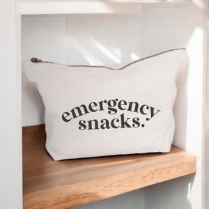 May include: A white canvas zippered pouch with the text "emergency snacks." printed in black.