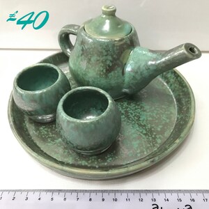 May include: A green ceramic tea set with a teapot, two cups, and a tray. The set has a speckled green glaze.