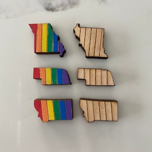 May include: Six wooden state outline shapes, three with a rainbow design and three with a natural wood finish. The states are Missouri, North Dakota, and Montana.