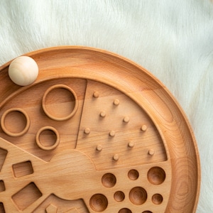 May include: A wooden toy with different shapes and patterns for children to explore. The toy has a circular base with a variety of cutouts, including circles, squares, and triangles. There are also pegs and holes for sorting and matching.