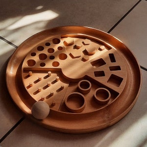 May include: A wooden tray with different shaped cutouts, including circles, squares, and geometric shapes. A wooden ball is sitting on the tray.