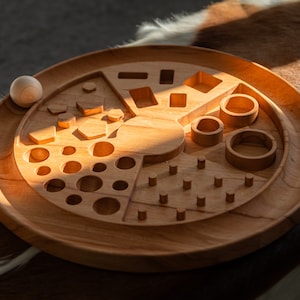 May include: A wooden toy with various shapes and sizes cut out of the surface. The toy is designed for a child to place wooden balls into the cutouts.