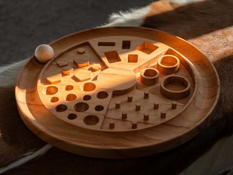 May include: A wooden toy with various shapes and sizes cut out of the surface. The toy is designed for a child to place wooden balls into the cutouts.