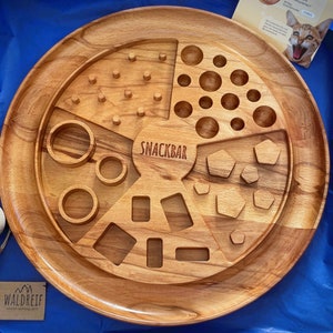 May include: A wooden snack board with various compartments for snacks. The board is divided into five sections, each with a different design. The center section features the word "Snack Bar".