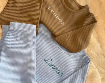 Könnte beinhalten: Zwei Pyjama-Sets, eines braun und eines hellblau, mit dem Namen "Lennox" bestickt.