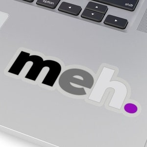 Op de afbeelding: Een sticker met het woord "meh" in zwarte, grijze en witte letters met een paarse stip.