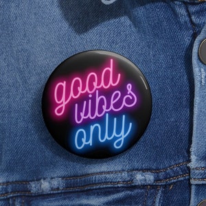 Könnte beinhalten: Ein schwarzer Knopf mit einem neonrosa und blauen Design, auf dem "good vibes only" steht.