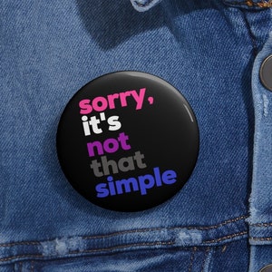 Op de afbeelding: Een zwarte knop met de tekst "sorry, it's not that simple" in roze, wit, grijs en blauwe letters.