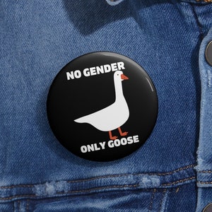 May include: A black and white button with a white goose and the text "NO GENDER ONLY GOOSE" on a denim jacket.