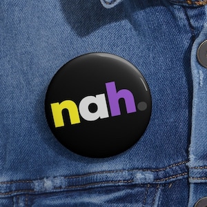 Op de afbeelding: Een zwarte knop met het woord "nah" in gele, witte en paarse letters. De knop is vastgemaakt aan een blauw denim jack.