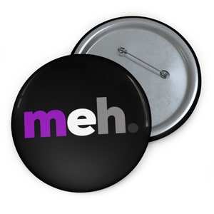 May include: A black button with a white background and the word "meh." in purple, white, and gray letters. The button has a silver pin on the back.