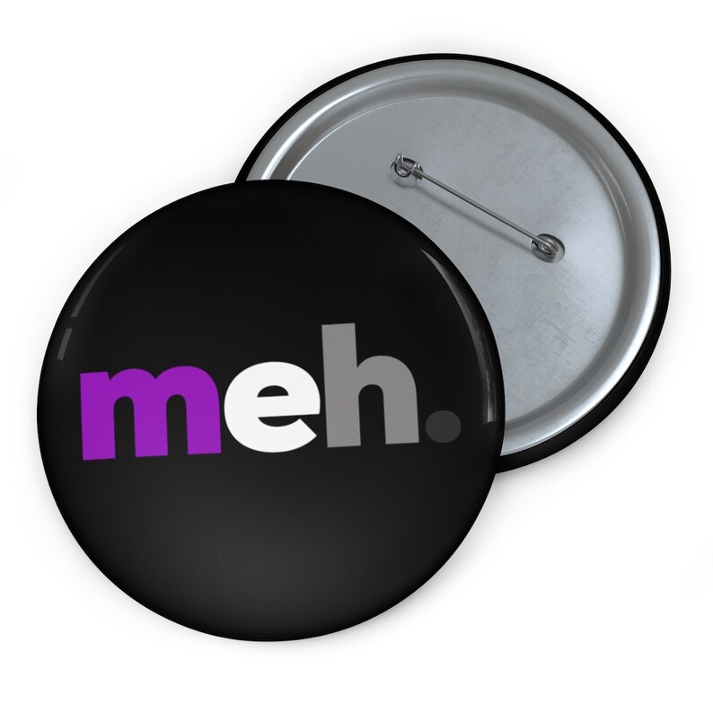 May include: A black button with a white background and the word "meh." in purple, white, and gray letters. The button has a silver pin on the back.